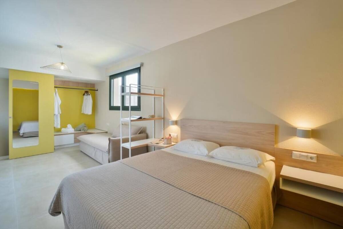 A modern hotel room with a large bed, bedside tables, a wardrobe, and a mirror.