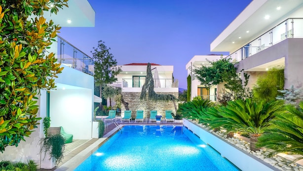 A modern pool area with a clear blue pool, green lounge chairs, and a stone wall backdrop. - Village Esperia  (Thasos)