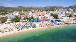 A coastal town with a beach lined with umbrellas and sun loungers, a clear blue sea, and buildings in the background. - Village Esperia  (Thasos)