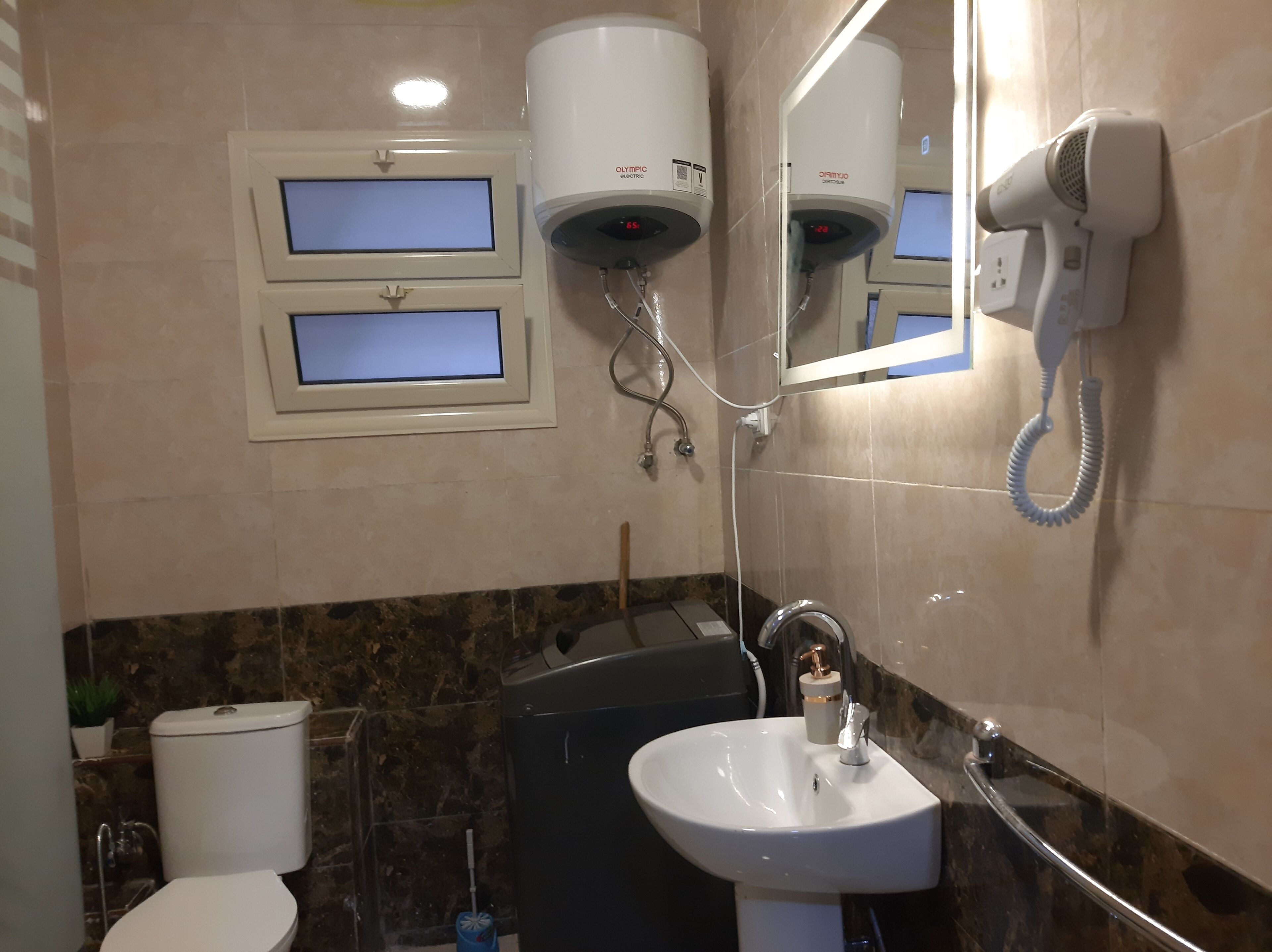 Et badeværelse med toilet, vask, spejl og to hårhærrere på væggen.