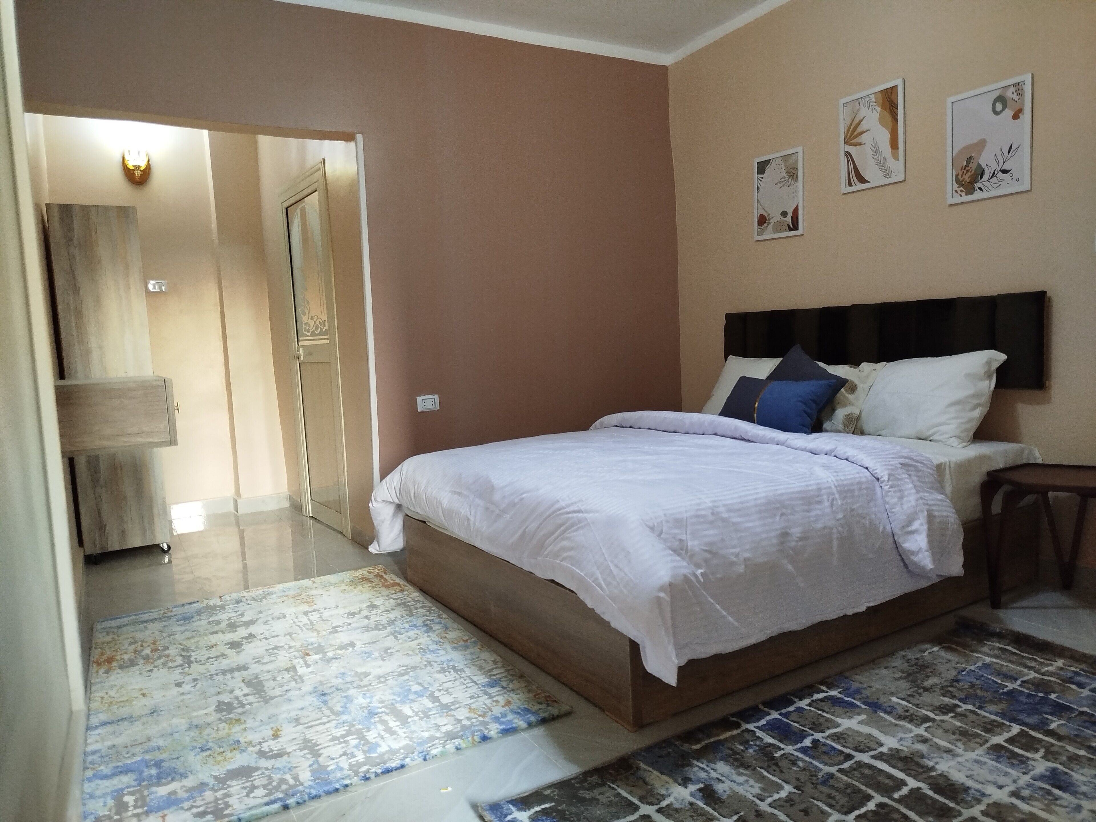 A bedroom with a bed, a nightstand, a wall-mounted TV, and a door leading to another room.
