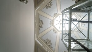 Una habitación con techos altos y decoraciones ornamentales, además de una barandilla de vidrio.