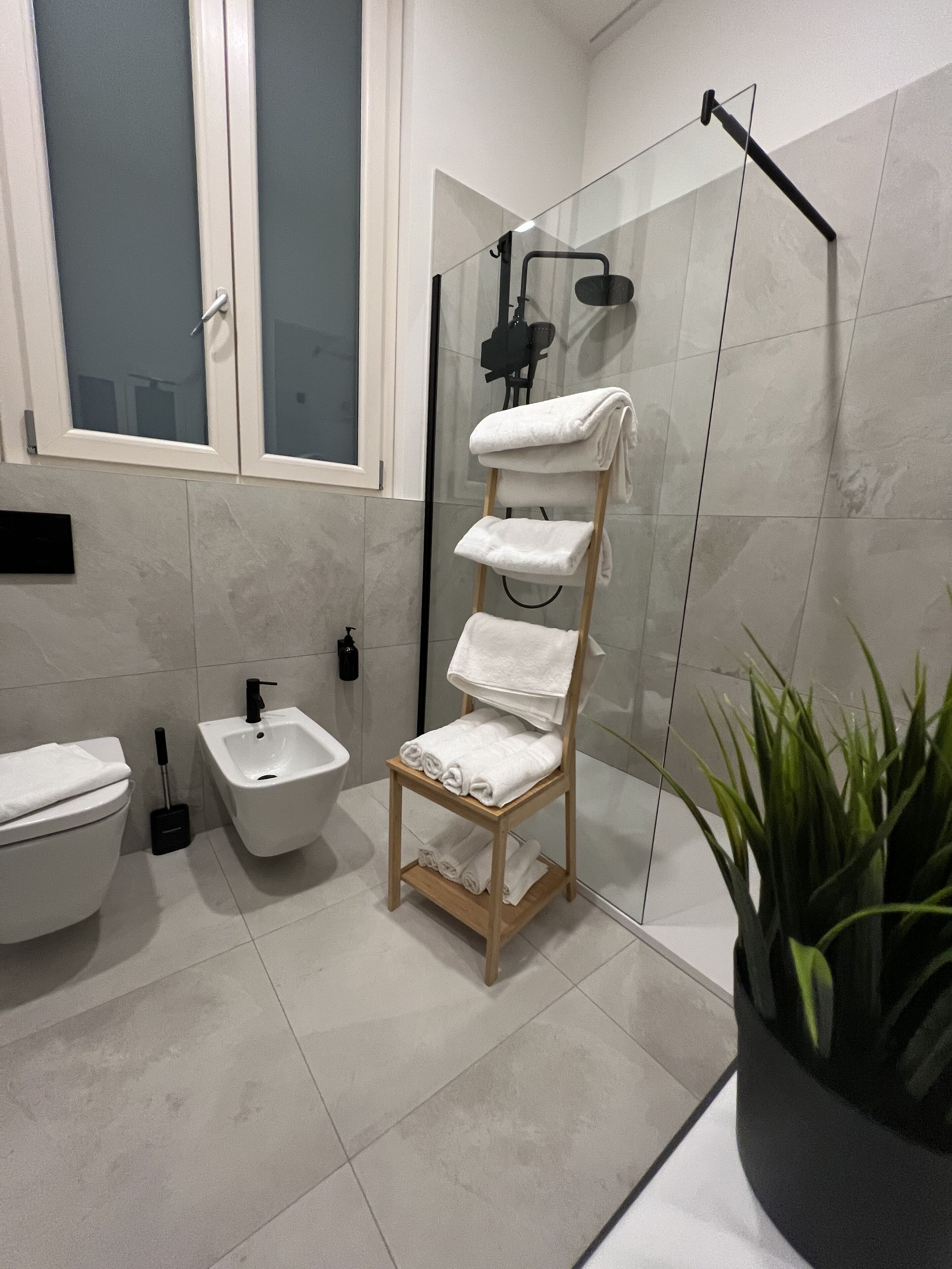 Un baño moderno con cabina de ducha de vidrio, un perchero de madera, un bidé y un inodoro.