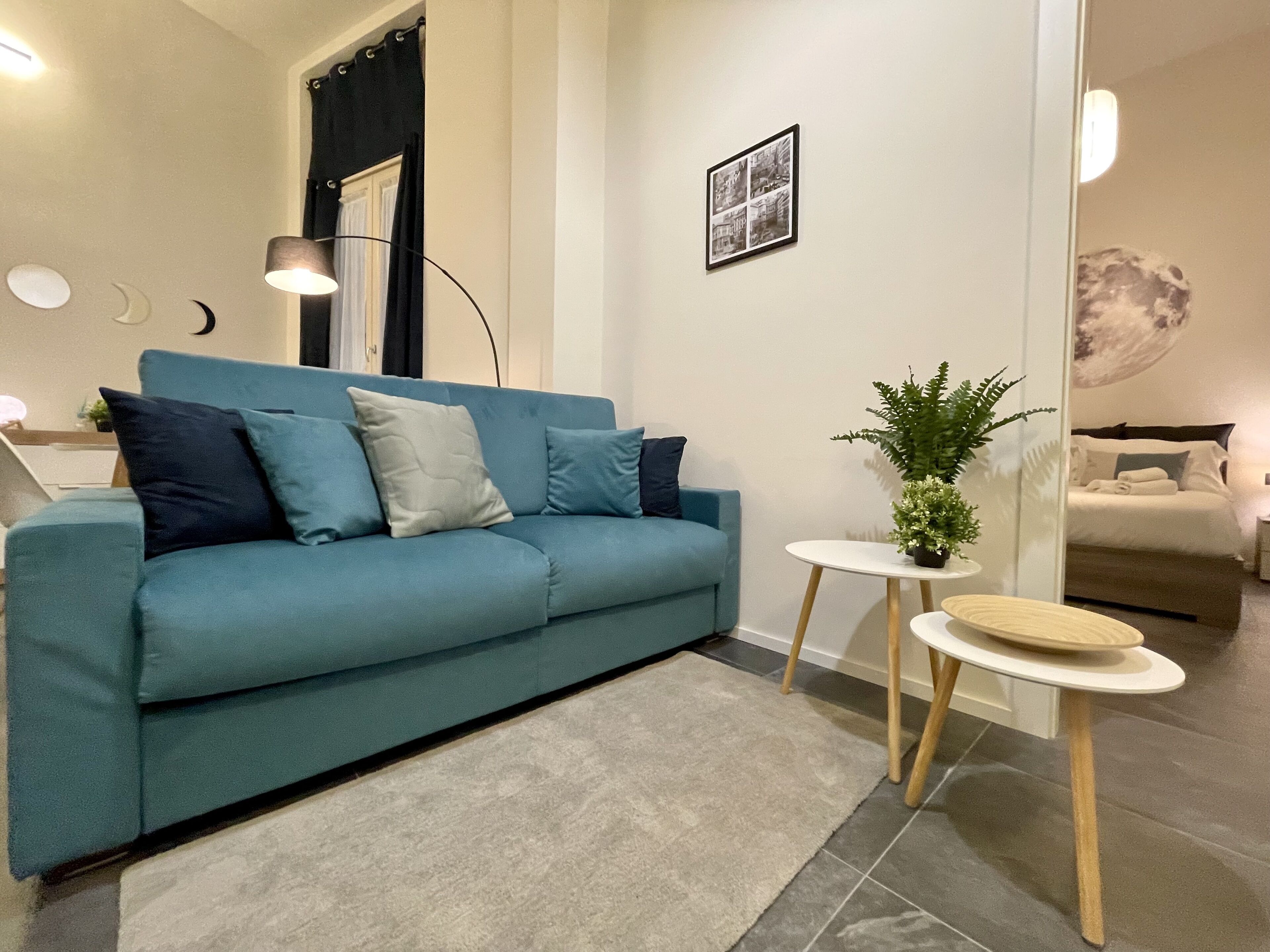 Een moderne woonkamer met een blauwgroene bank, een klein rond tafeltje met een plant, en een ingelijst beeld aan de muur.