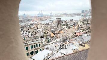 Vista di una zona urbana densamente popolata, con diversi edifici, tra cui residenziali e commerciali, e un porto sullo sfondo con imbarcazioni e gru.