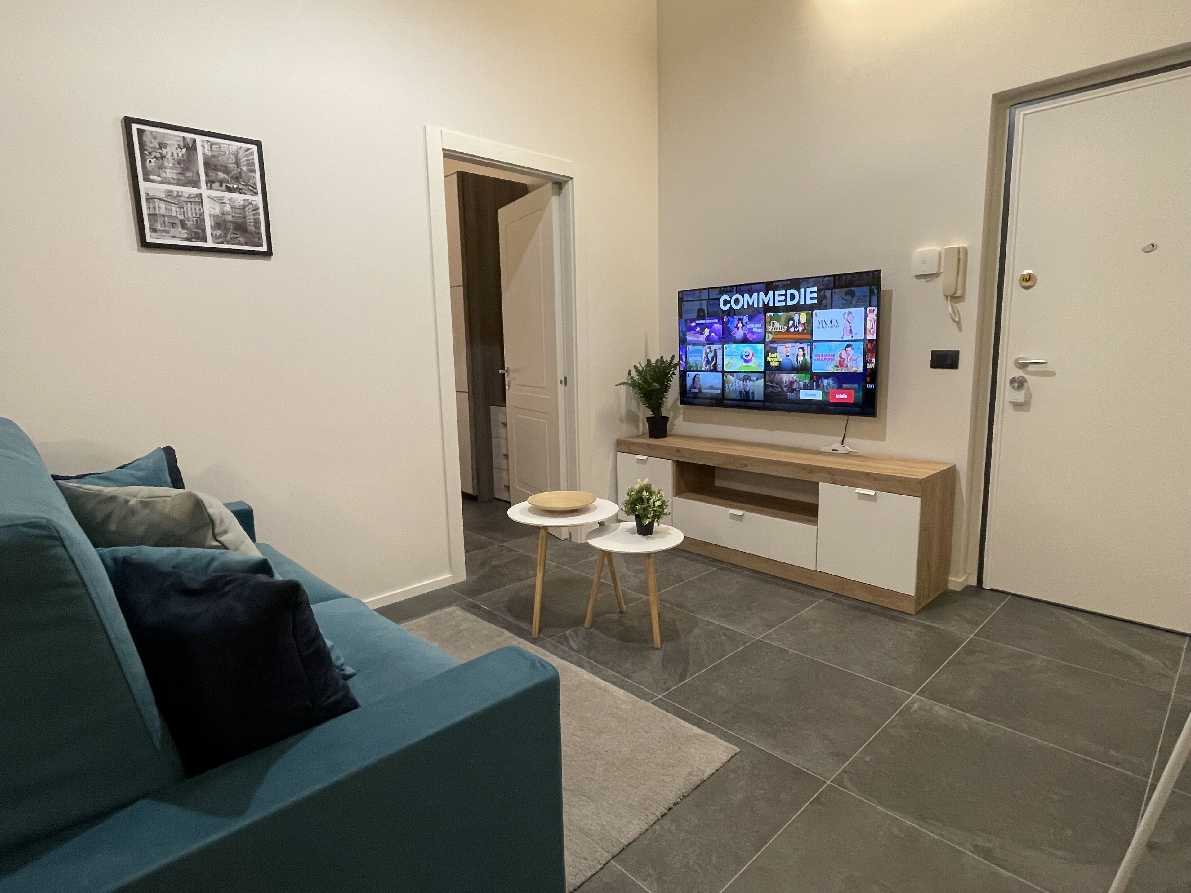 Una sala de estar moderna con un sofá azul, un televisor montado en un mueble de madera y una mesita con una planta.