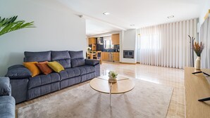Una sala moderna con un sofá gris, una mesita de centro redonda y una cocina al fondo.