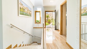 Un interior moderno con una escalera, piso de madera y vistas a un jardín a través de una puerta abierta.