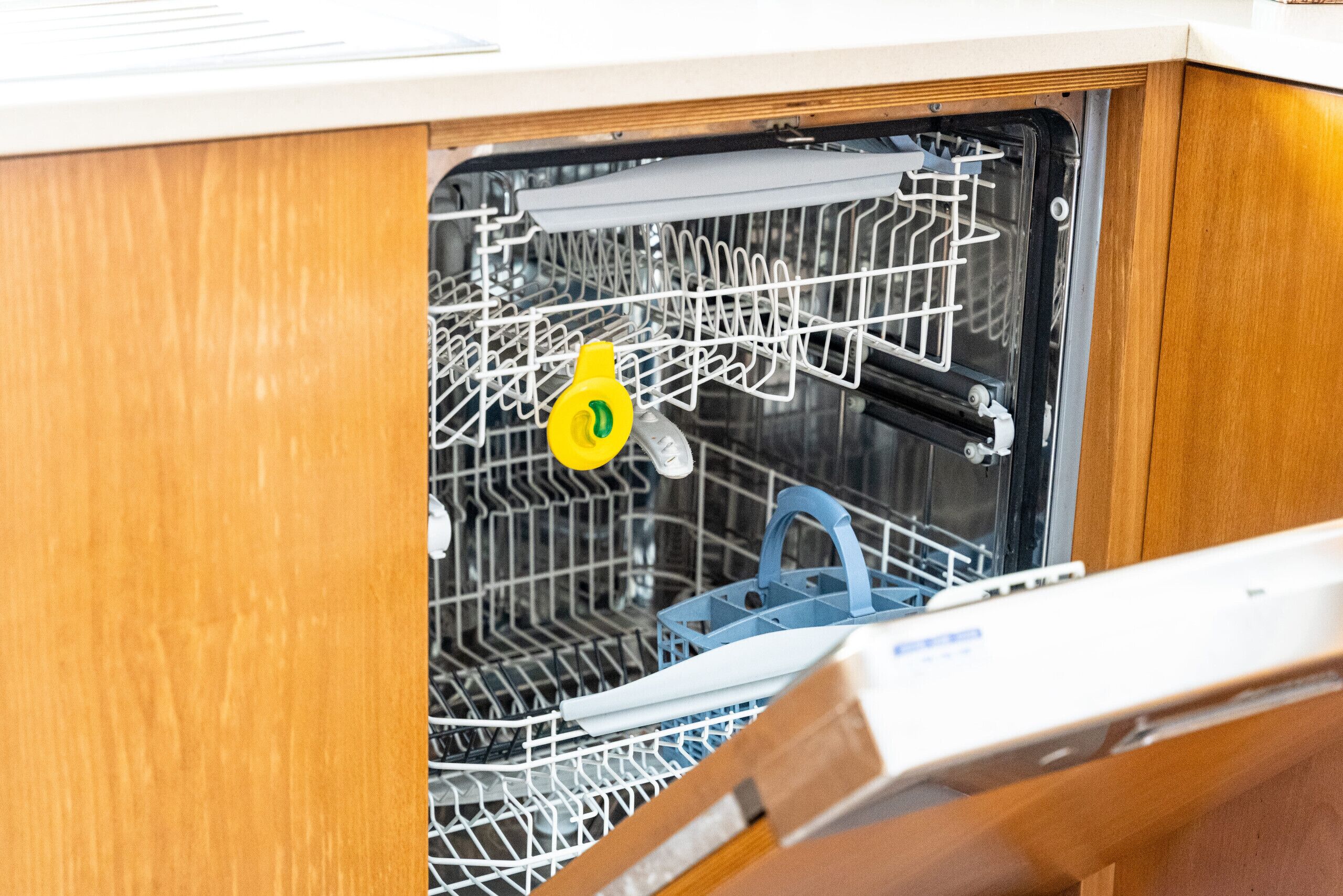 Màquina d'esbandir oberta amb una ampolla de detergent groga i un escorredor de plats blau a l'interior.