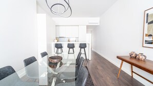 Ein moderner Essbereich mit einem Glastisch und Stühlen, einer hölzernen Bank sowie einer Küche im Hintergrund.