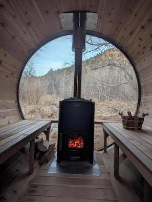 A circular wooden cabin with a wood-burning stove, benches, and a view of the surrounding forest. - Near National Parks, hot tub & sauna. Sleeps 30 (Glendale)