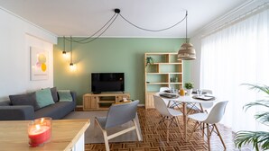Una sala de estar moderna con un sofá, televisor, mesa de comedor, sillas y una estantería.