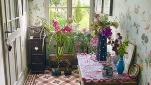 Un pasillo estrecho con baldosas estampadas, una máquina de escribir antigua y arreglos florales sobre una mesa.