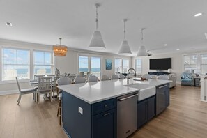 A modern kitchen with a central island, pendant lights, and a dining area with chairs and a table.