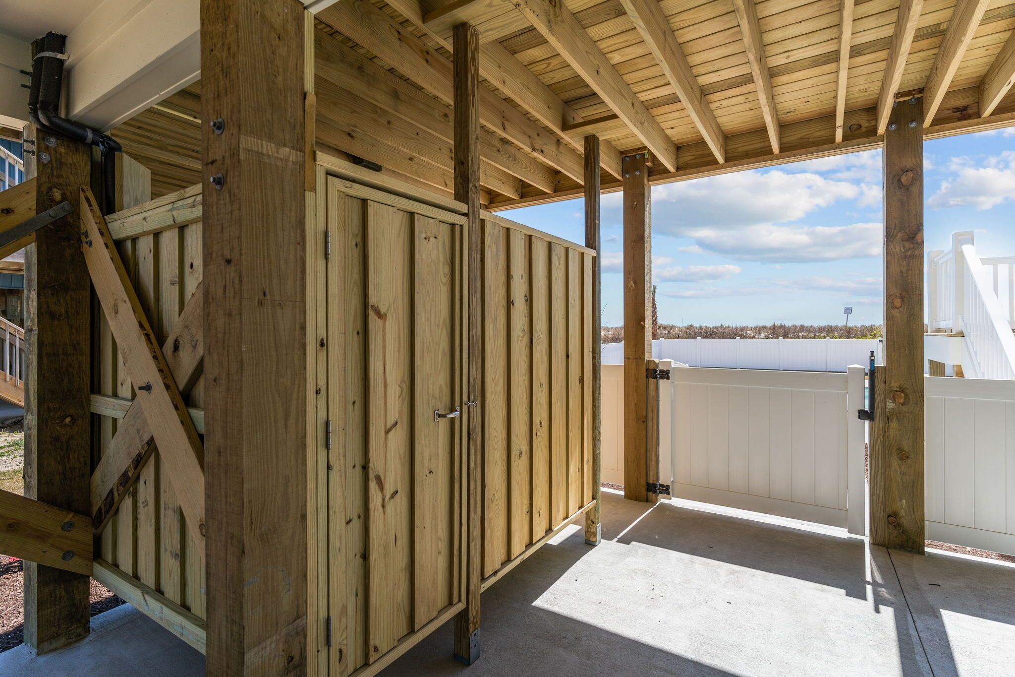 A wooden structure with a covered porch, a white fence, and a view of a body of water.
