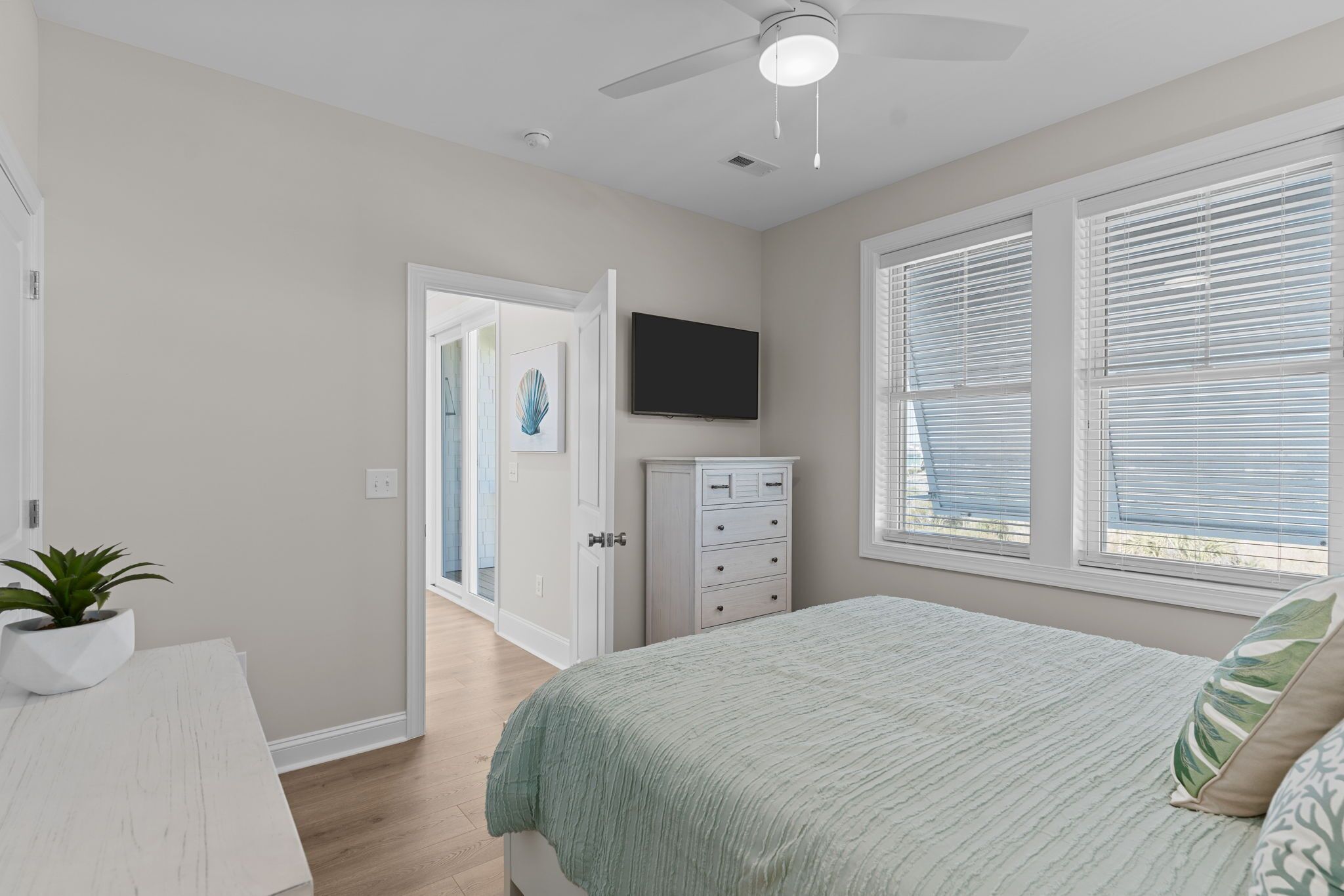 Un dormitorio con cama, ventilador de techo, televisor y ventana con persianas.