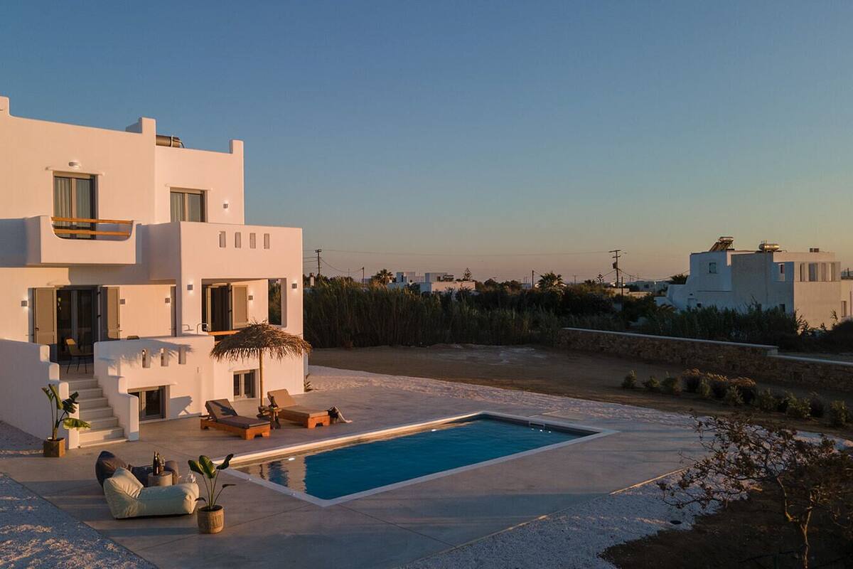 A modern white villa with a swimming pool, outdoor seating, and a view of the surrounding landscape.