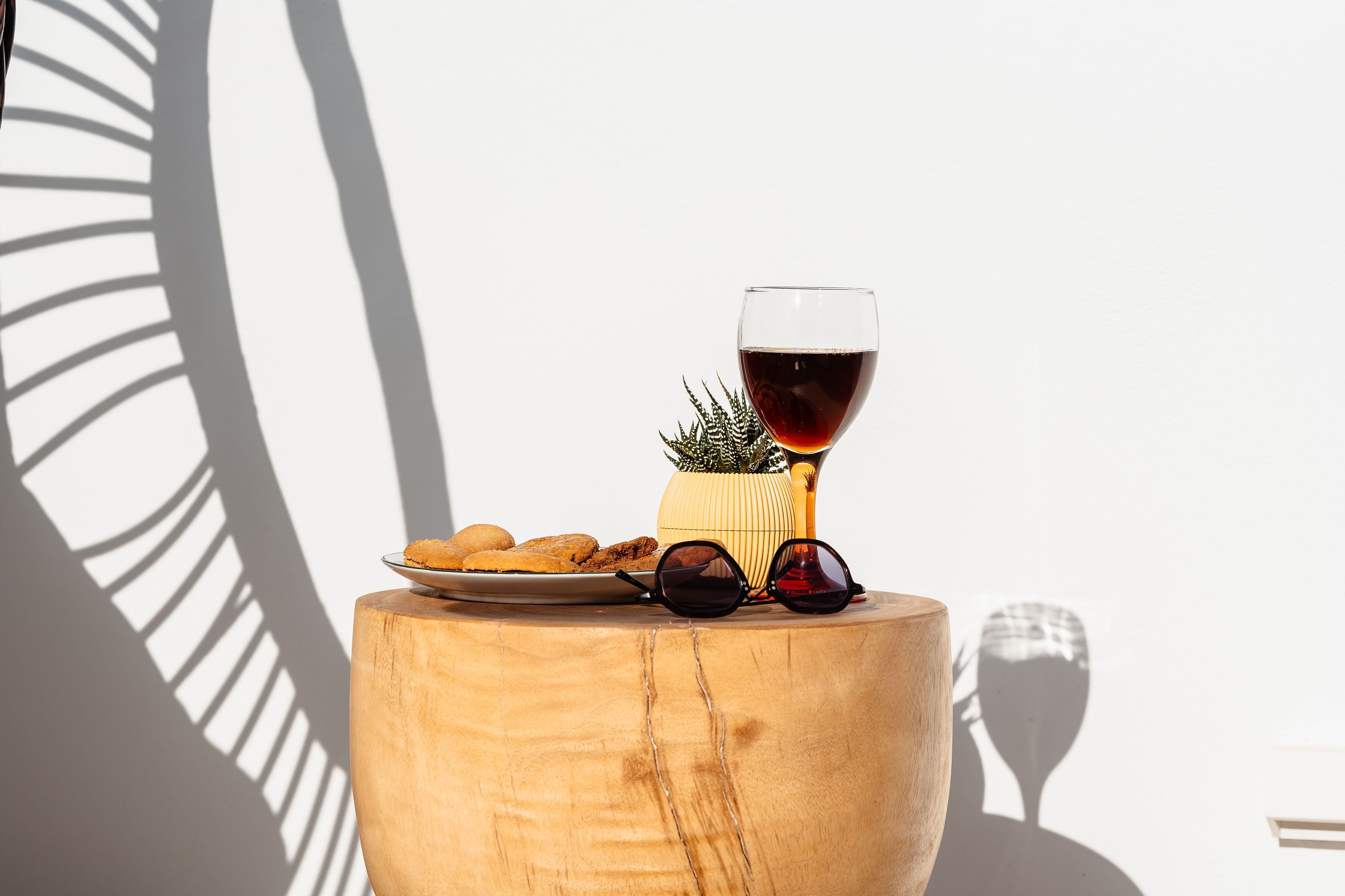 A wooden table with a glass of red wine, sunglasses, and a plate of food.
