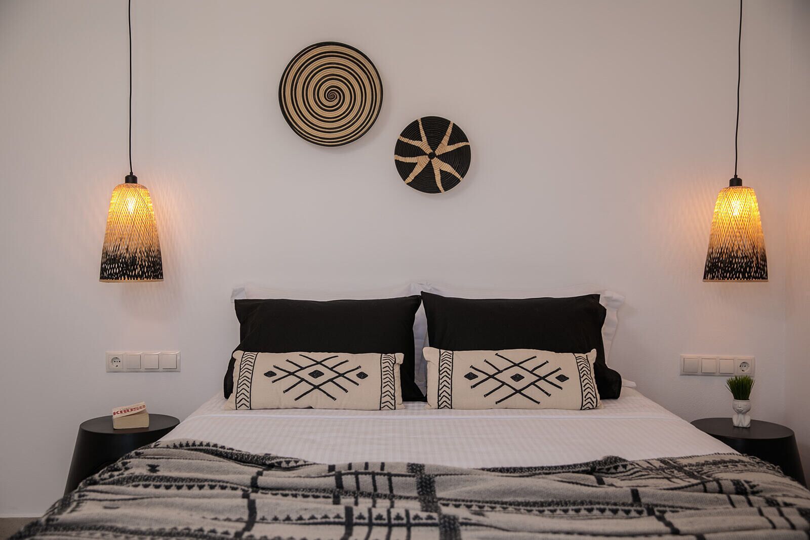 A neatly made bed with patterned pillows, two wall-mounted light fixtures, and two decorative wall hangings.