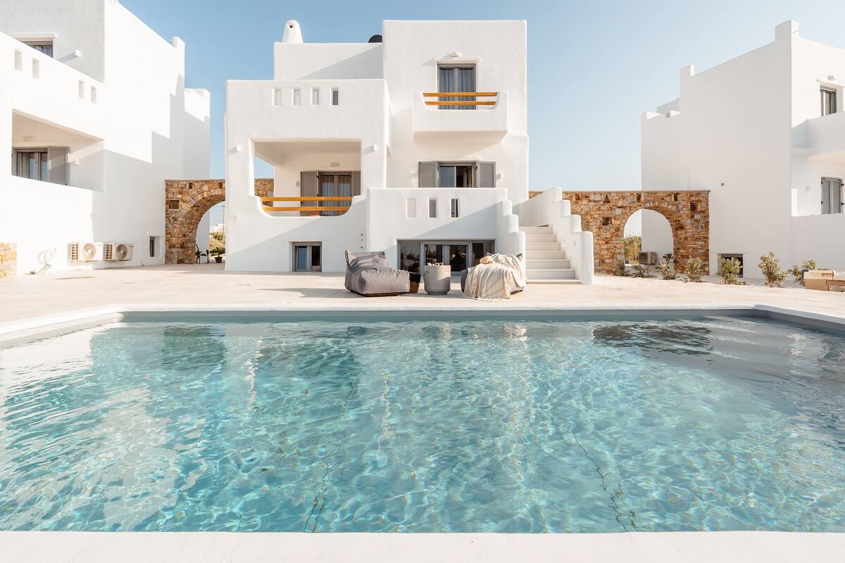 A modern white building with a swimming pool, stone archways, and outdoor seating.