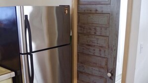 Una cocina con un refrigerador de acero inoxidable, una puerta de madera y suelo de baldosas.
