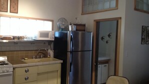 Cocina compacta equipada con refrigerador, estufa y microondas. Incluye gabinetes y un lavamanos.