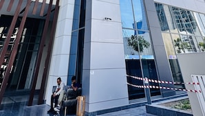 Un immeuble moderne de grande hauteur, doté d’une façade en verre, d’une entrée imposante avec un portail de sécurité et d’une borne d’incendie bien visible au niveau du sol.