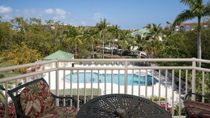 A balcony with a pool view, outdoor seating, and lush greenery. - Sunrise 307-2BR/2BA condo near beaches with pool, parking, balcony (Key West)