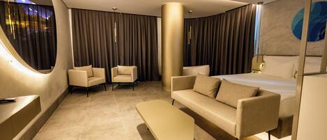 Una habitación de hotel moderna con una pared curva, una cama grande, un sofá, una silla y una mesita.