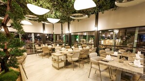 Un restaurant moderne avec un plafond haut, des luminaires suspendus et une vue sur la ville grâce à de grandes fenêtres.