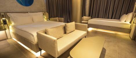 Une chambre d’hôtel moderne avec un grand lit, un canapé, une petite table et une grande fenêtre avec des rideaux.