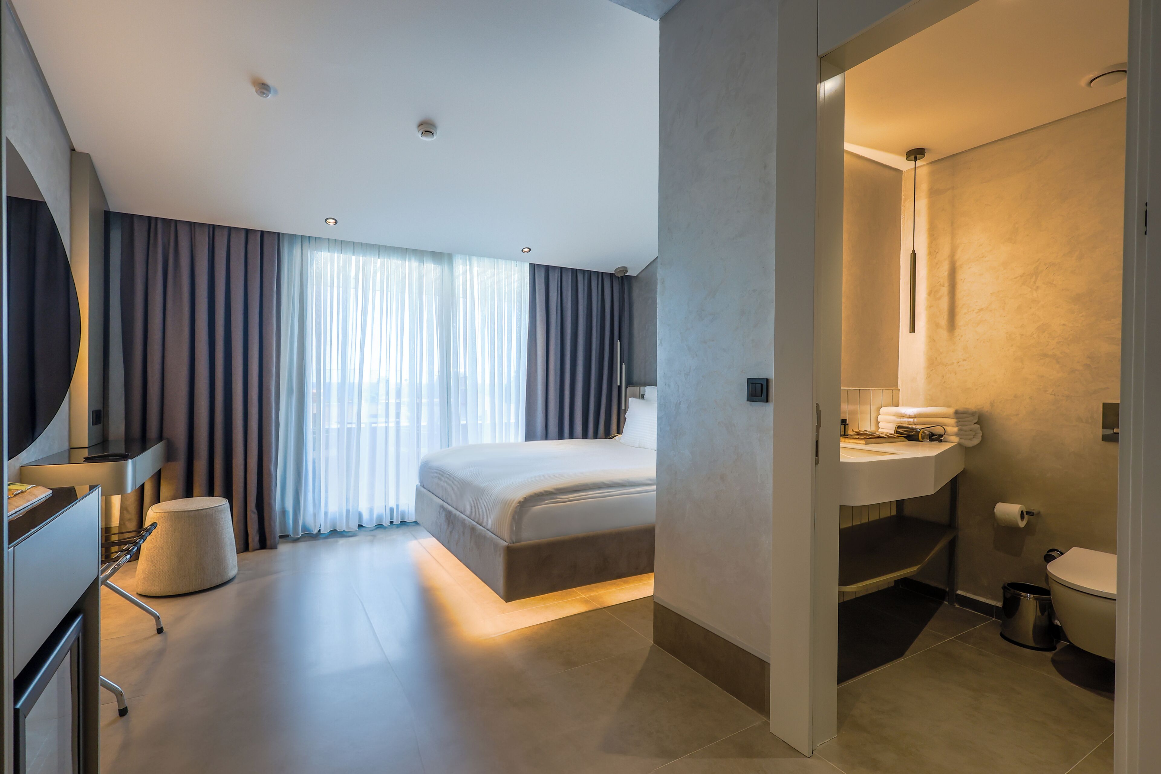 A modern hotel room with a large bed, a desk, and a bathroom with a sink and toilet.