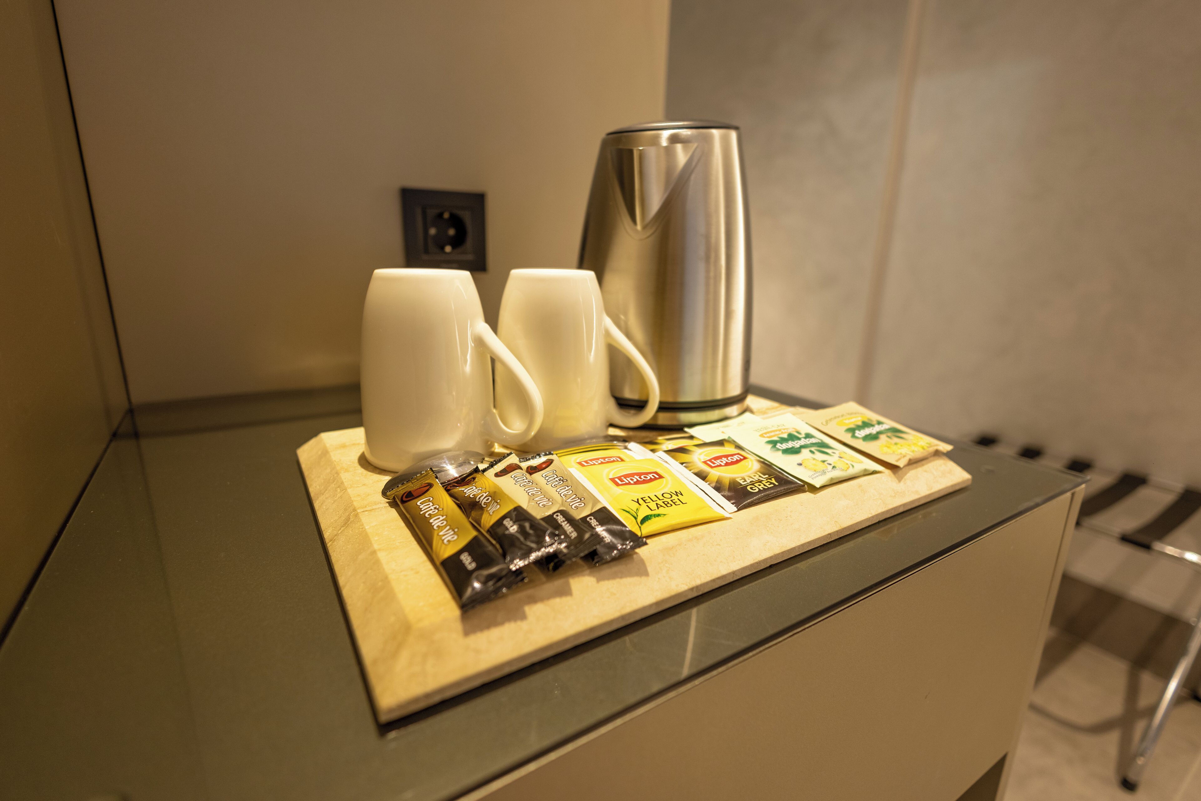 A kitchenette with a coffee maker, two mugs, and tea packets on the counter.
