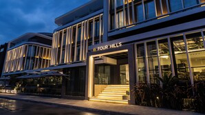 Un hôtel moderne doté d’une façade en verre, d’une terrasse et d’une enseigne indiquant « FOUR HILLS HOTEL ».