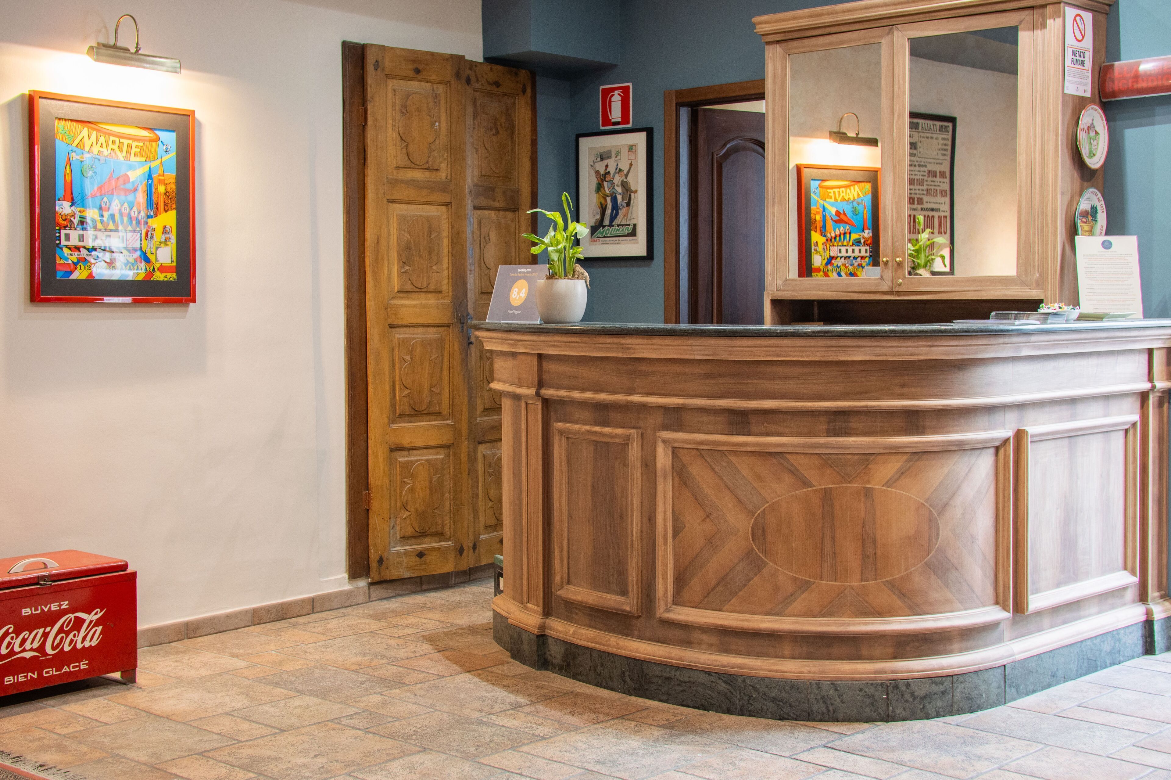 A reception desk with a wooden finish, a potted plant, framed artwork, and a Coca-Cola cooler.