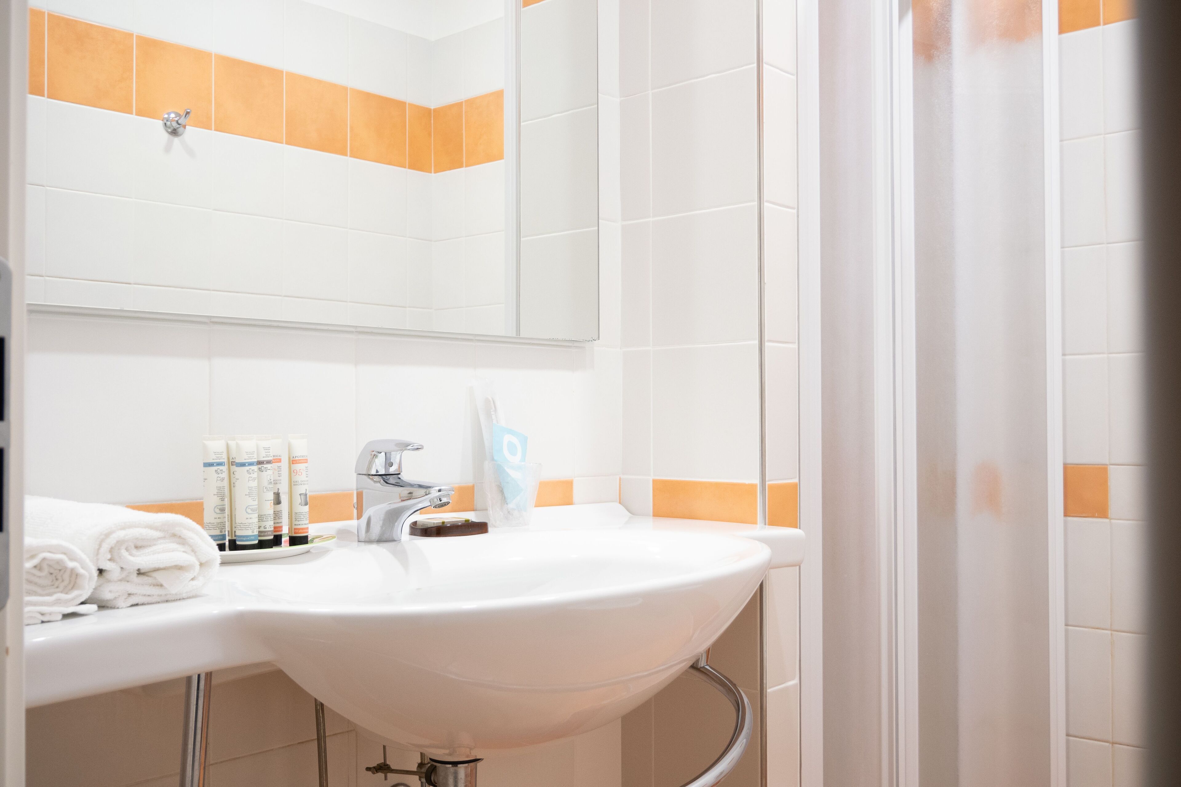 Een badkamer met een wit wastafel, spiegel en wandtegels in oranje tint.