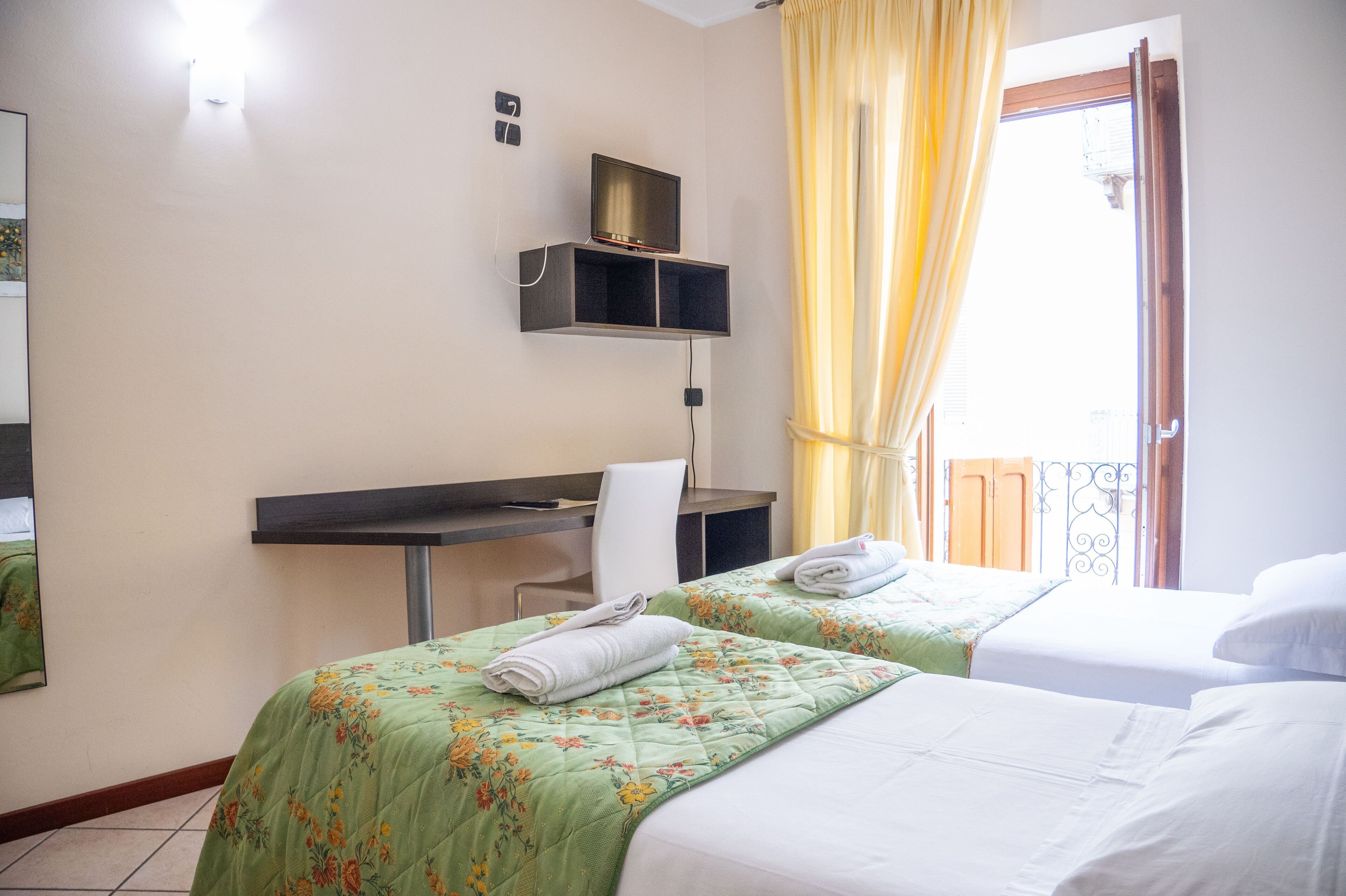 Una habitación de hotel con dos camas, un escritorio, una silla y un televisor en un estante.