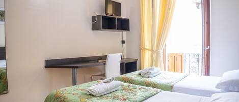 Ein Hotelzimmer mit zwei Betten, einem Schreibtisch, einem Stuhl und einem Fernseher auf einem Regal.