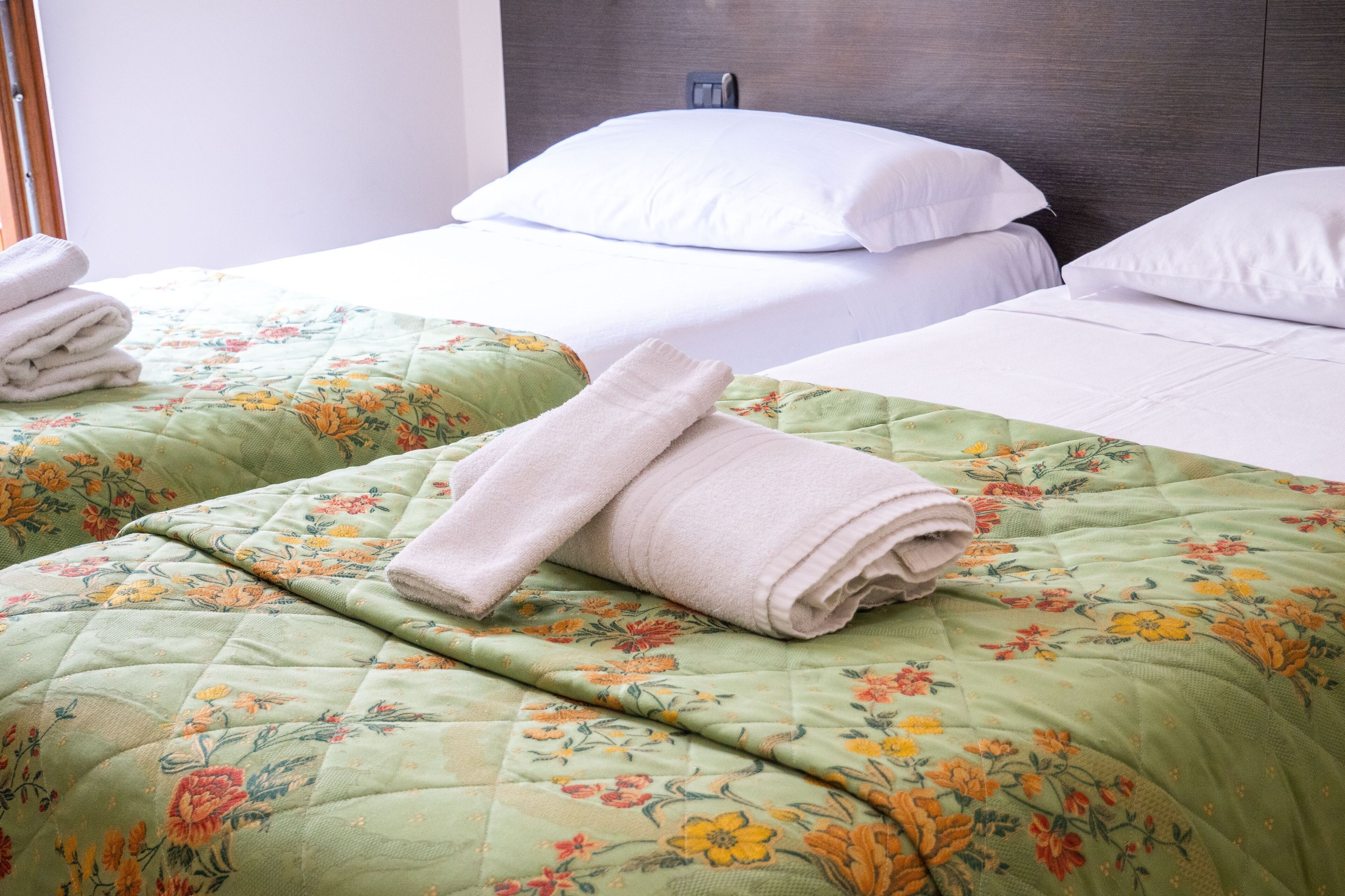 Una habitación de hotel con dos camas, cada una con ropa de cama estampada con motivos florales y toallas dobladas con cuidado.
