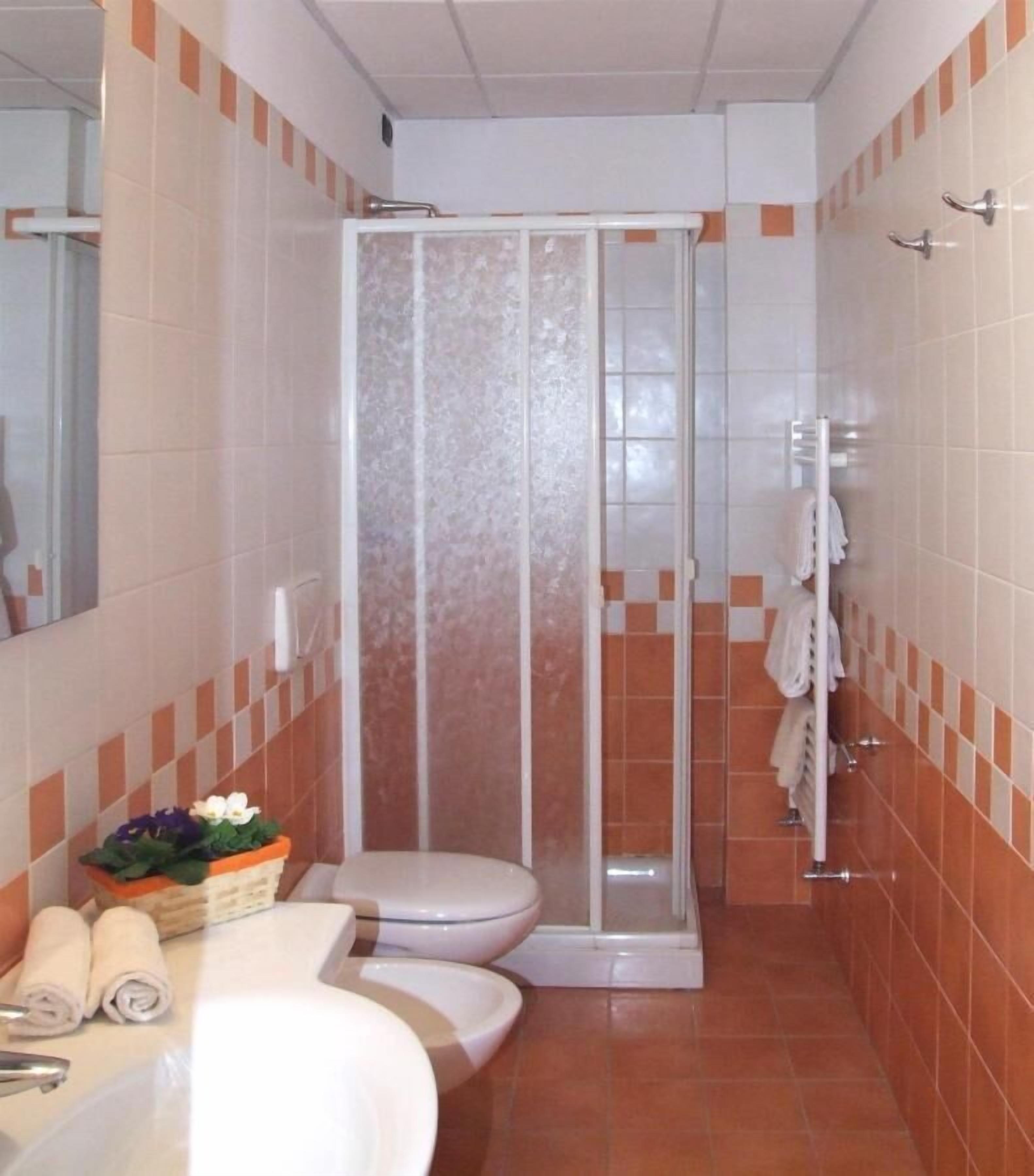 A bathroom with a shower enclosure, toilet, sink, and a towel rack.