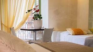 Habitación de hotel con cama, mesita de noche con planta en maceta, silla y vista al balcón exterior.