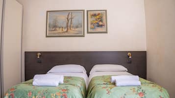 Ein Hotelzimmer mit zwei Einzelbetten, jeweils mit floralem Bettbezug und weißen Kissen, einem dunklen Kopfteil und zwei gerahmten Bildern an der Wand.
