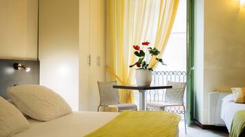 Quarto de hotel com uma cama, uma mesa pequena com uma planta em vaso, varanda com cortinas amarelas e vista para o exterior.