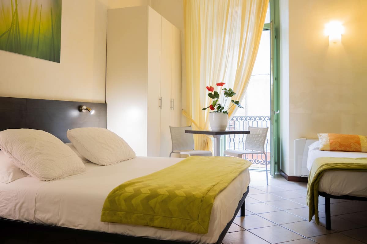 Ein Hotelzimmer mit Bett, einem kleinen Tisch mit Blumenvase, einem Sessel und einem Balkon mit Geländer.