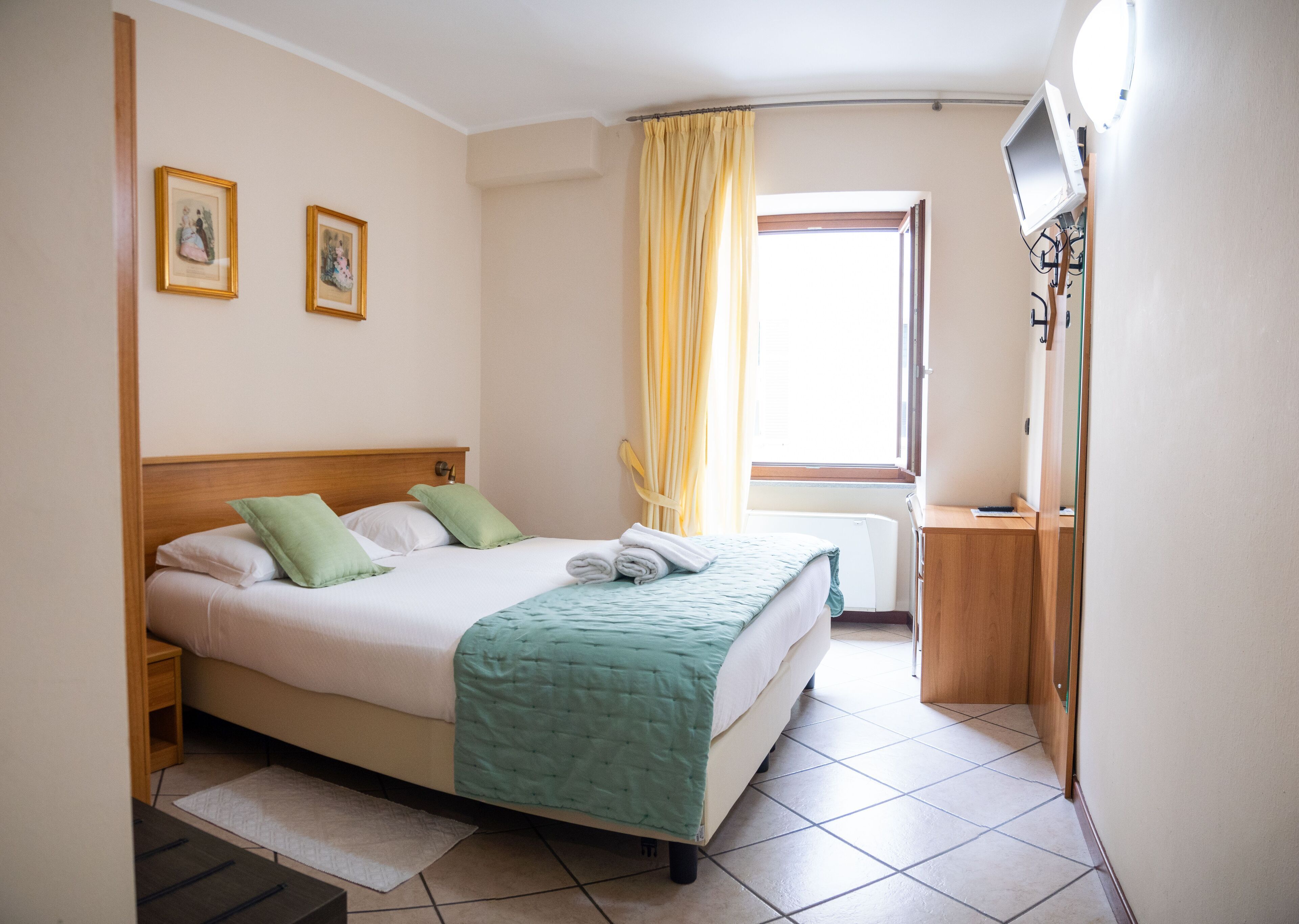 Una habitación de hotel con cama, mesita de noche, espejo y ventana con cortinas.