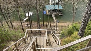 Una scala di legno conduce a un molo sull'acqua, circondato da alberi e da un piccolo edificio con tetto blu.