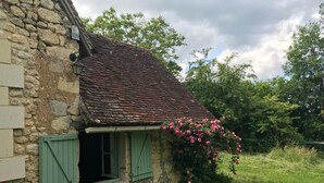 A rustic stone house with a sloped roof, a small window with green shutters, and a wall-mounted light fixture. - Maison Nature Dans le Perche, à 100 m de la Forêt de Bellême (Belforêt-en-Perche)