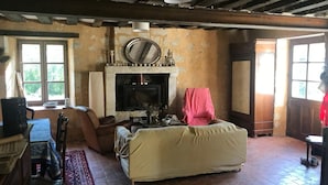 A rustic room with a fireplace, a sofa, a chair, and a table. - Maison Nature Dans le Perche, à 100 m de la Forêt de Bellême (Belforêt-en-Perche)