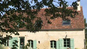 A rustic building with a brick roof, green shutters, and a small balcony. - Maison Nature Dans le Perche, à 100 m de la Forêt de Bellême (Belforêt-en-Perche)