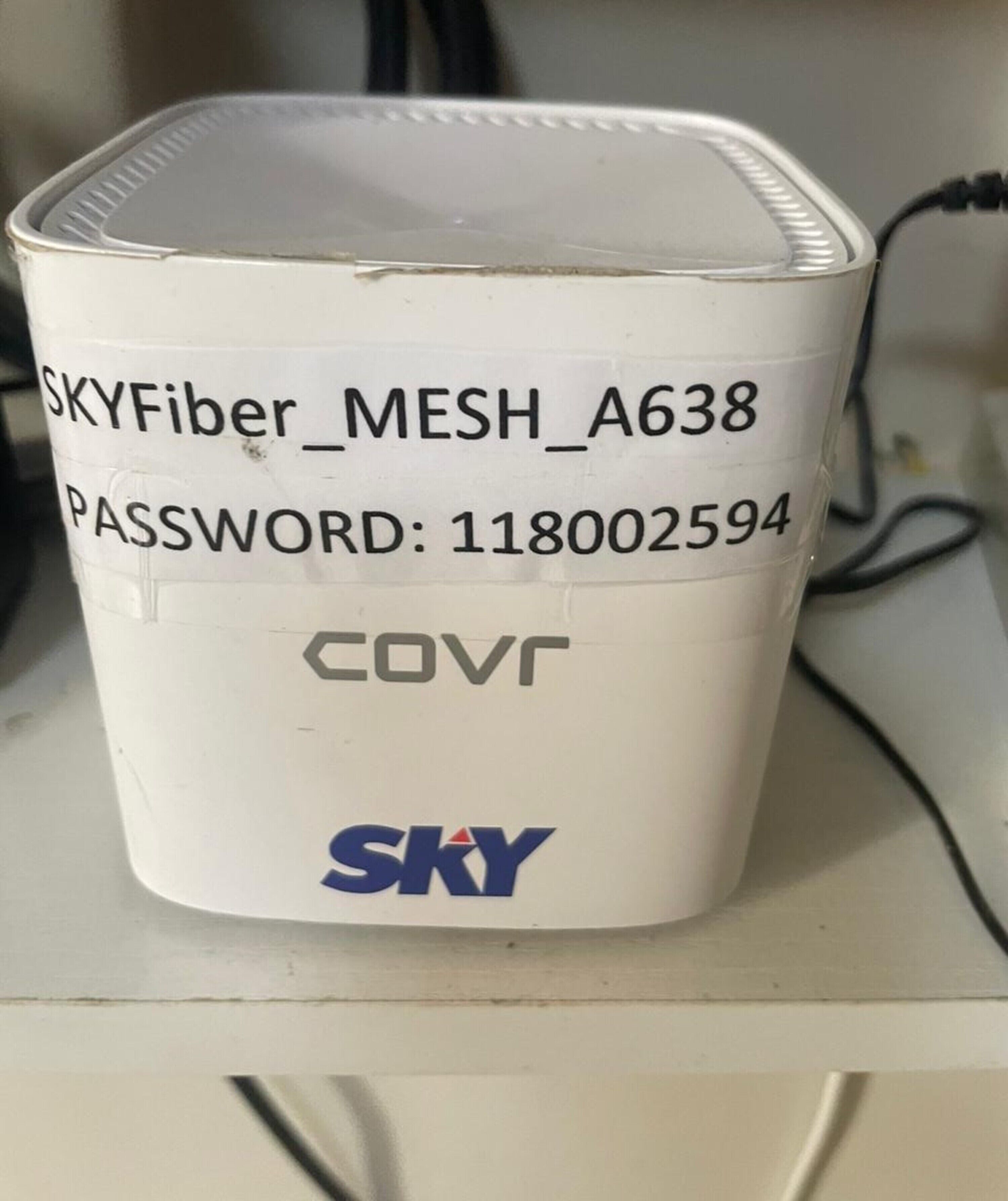 En hvid, cylinderformet enhed med tekst og logoer, herunder "SKYFiber_MESH_A638" og "SKY" nederst.